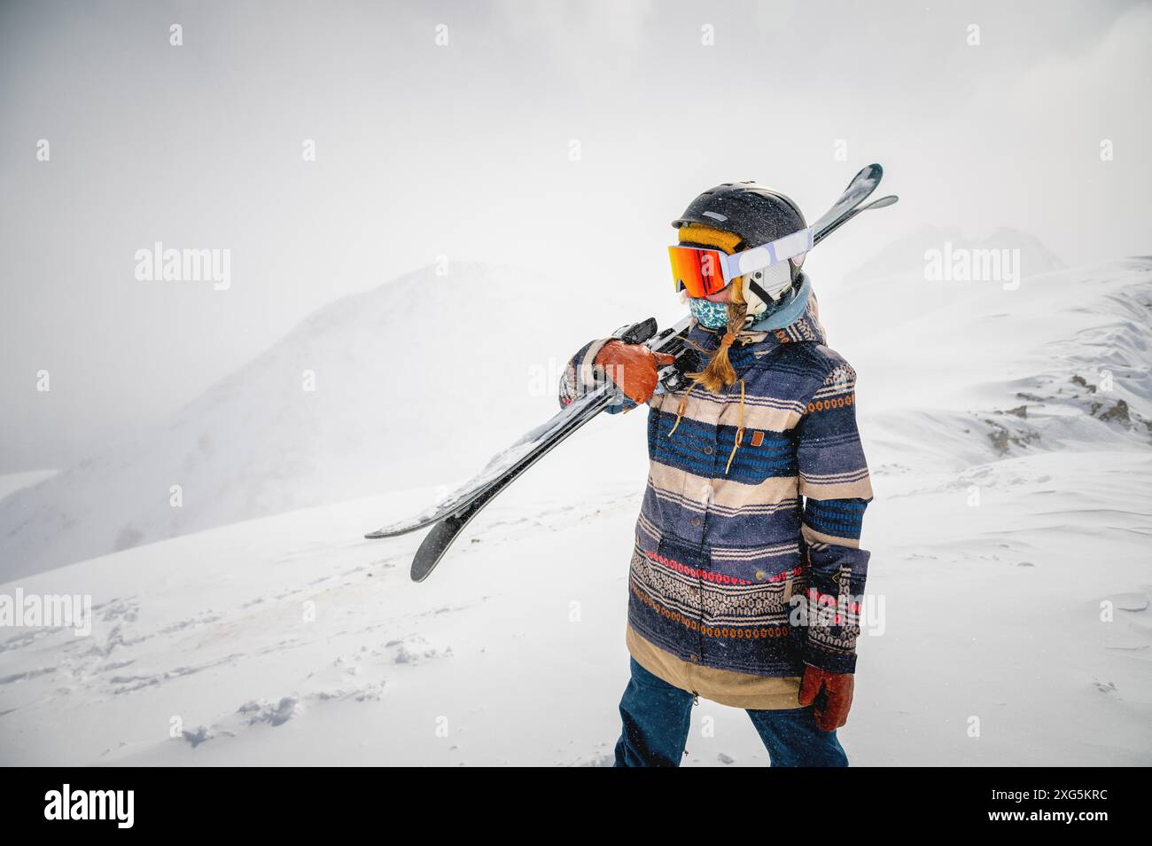 Porträt einer hübschen und aktiven Skifahrerin, die eine Maske trägt und Ski in der Hand hält, aktive Winterferien. Extreme Lifestyle-Konzept Stockfoto