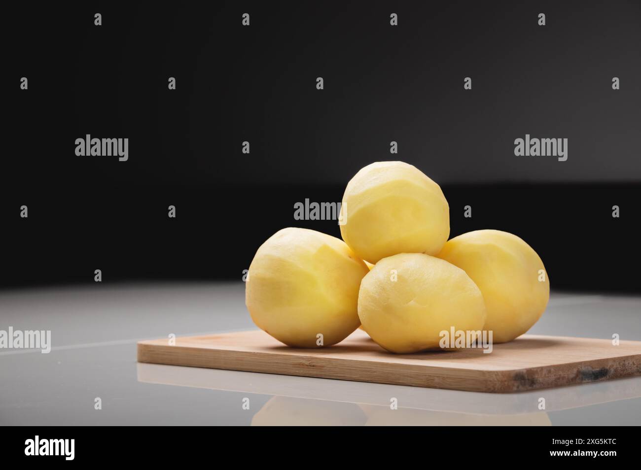 Geschälte, klassische Bratkartoffeln auf einem hölzernen Schneidebrett auf einem weißen Tisch. In einem dunklen Kochraum Stockfoto