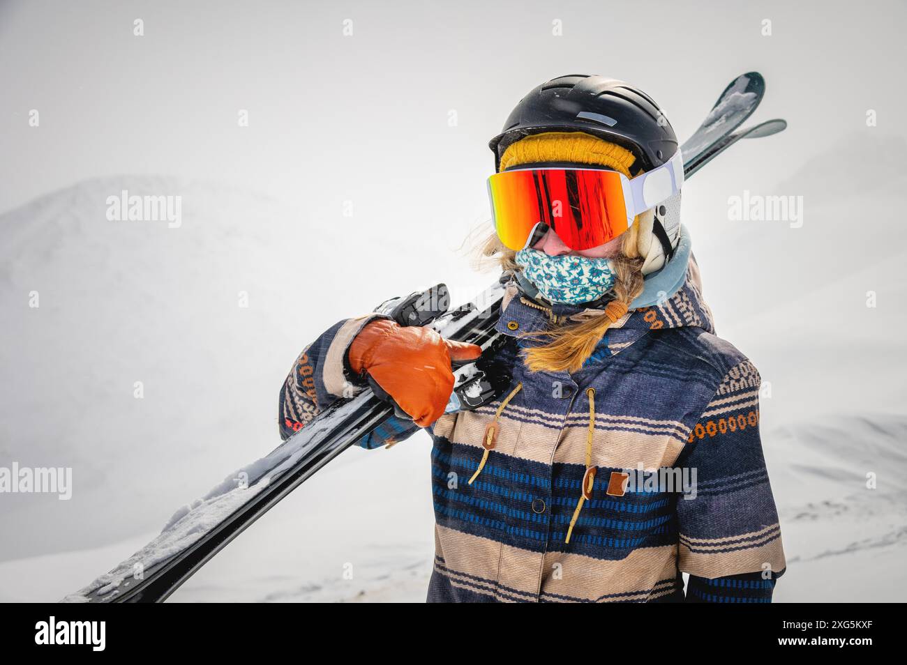 Porträt einer hübschen und aktiven Skifahrerin, die eine Maske trägt und Ski in der Hand hält, aktive Winterferien. Extreme Lifestyle-Konzept Stockfoto
