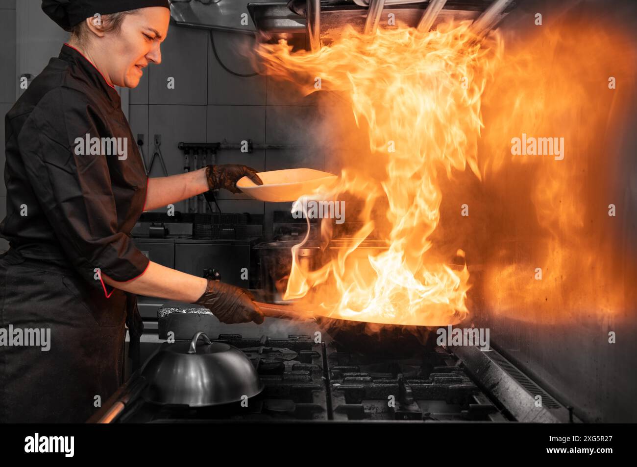 Die Küchenchefin kocht Wok in der Küche. Kochen flammender Wok mit Gemüse in der kommerziellen Küche. Hochwertige Fotografie Stockfoto