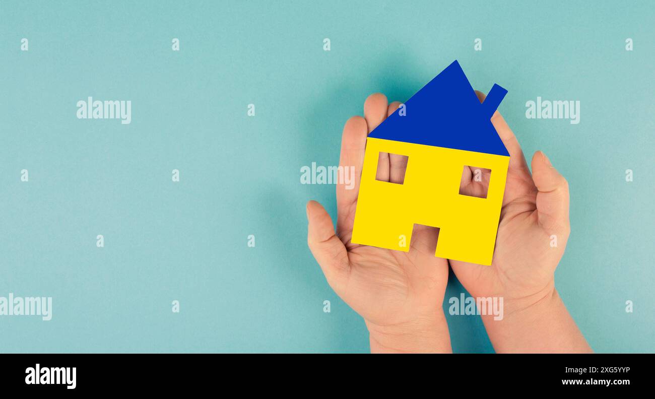 Ein Haus in der Hand mit den Farben der ukrainischen Flagge halten, Heimat für Flüchtlinge aus der Ukraine, Hilfe für Familien Stockfoto