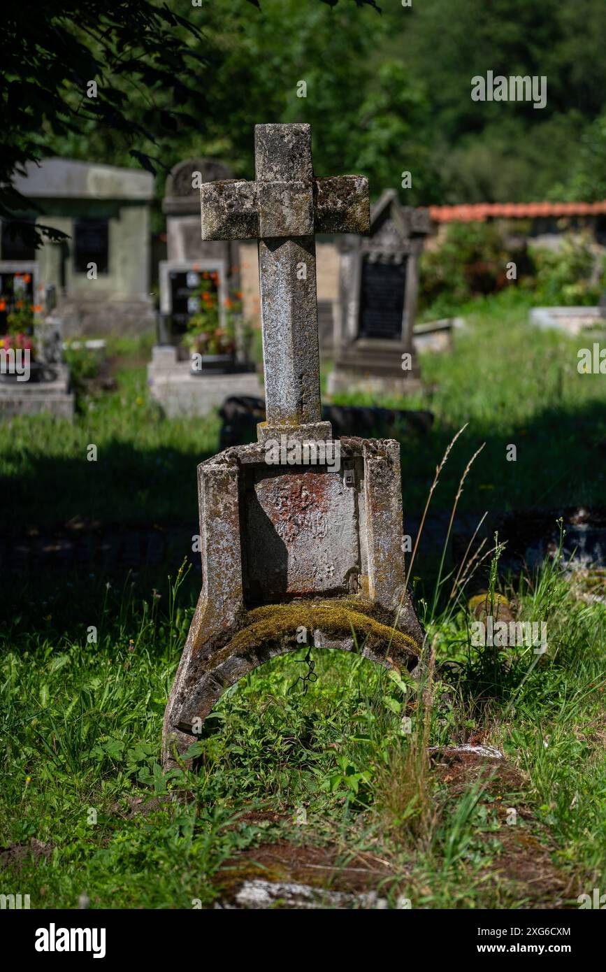 Altes Grab mit Kreuz und Bogen auf dem Friedhof des Dorfes Třebušice in Tschechien. Grünes Gras und andere Gräber im Hintergrund. Stockfoto