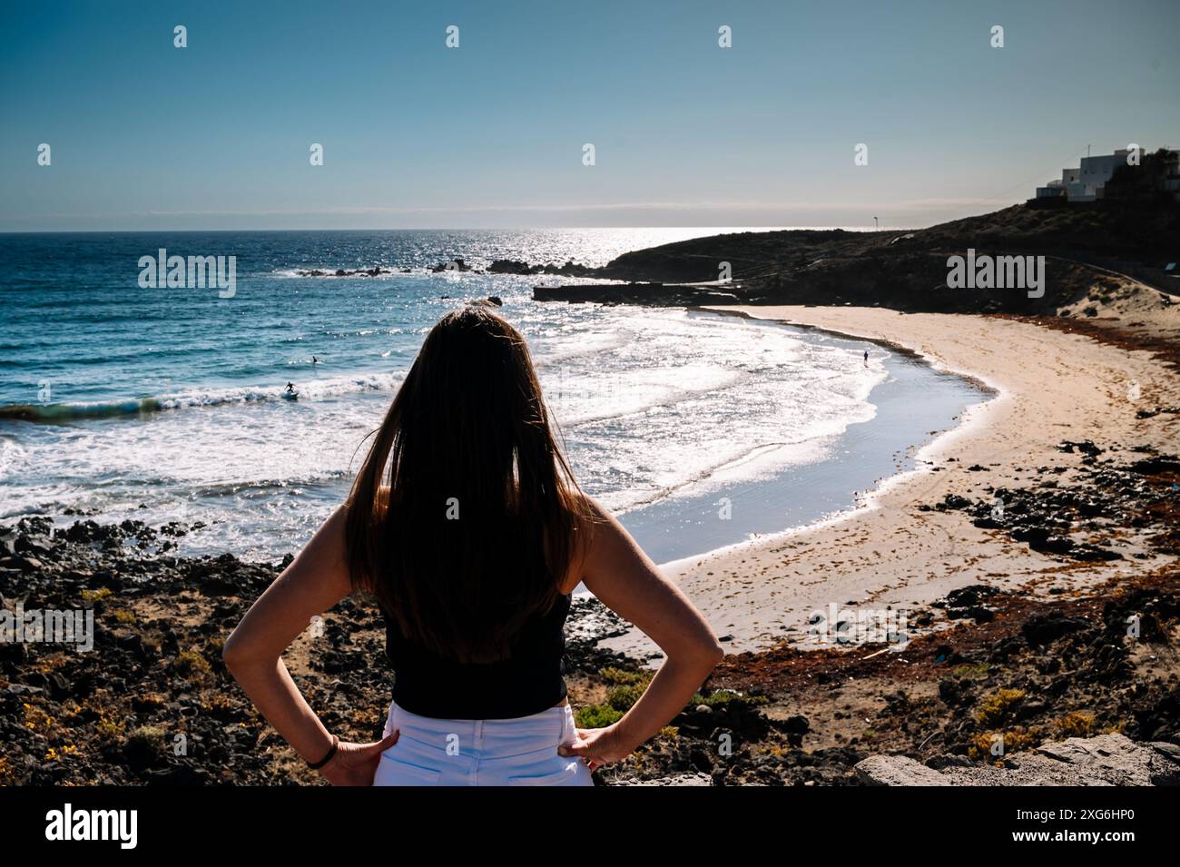 Eine Frau steht am Strand und blickt auf das Meer. Der Himmel ist klar und das Wasser ist ruhig Stockfoto