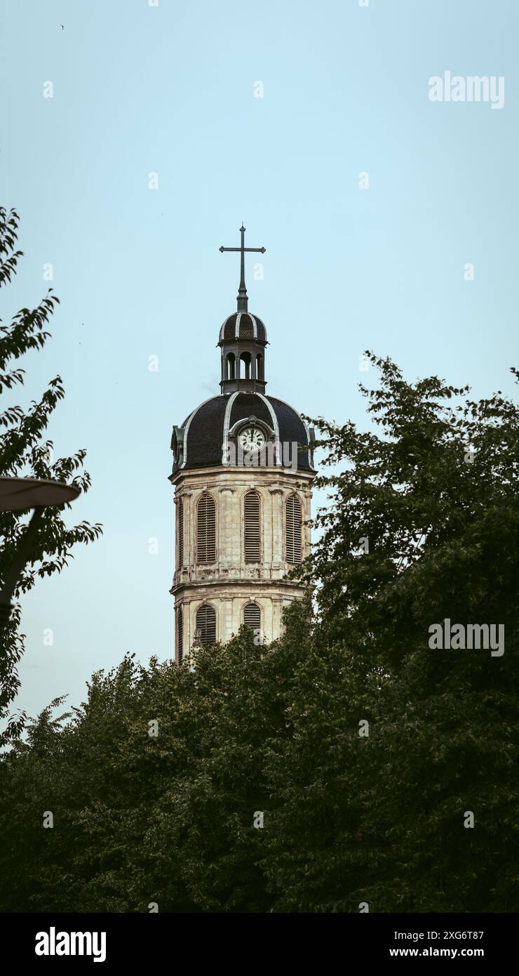 Ein Kirchturm mit einem Kreuz, eingerahmt von üppigen grünen Blättern. Es unterstreicht die friedliche Koexistenz von Architektur und Natur und bietet ein ruhiges und ruhiges Ambiente Stockfoto