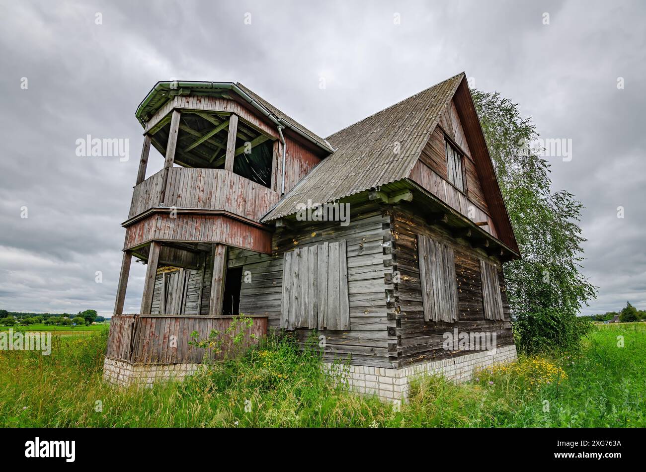 Altes hölzernes Bauernhaus in der litauischen Landschaft mit Sturmwolken am Himmel. Es gibt eine kurze Graswiese um das Haus herum. Stockfoto