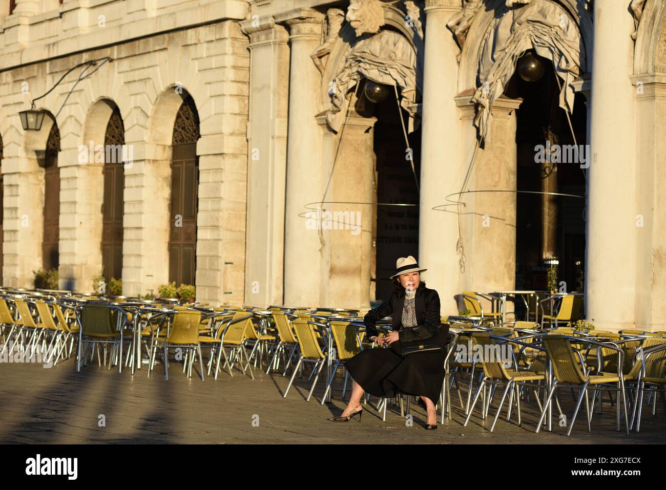 Eine glamouröse, gut gekleidete Frau sitzt in einem leeren Café im Freien und genießt am frühen Morgen die Aussicht auf Venedig Stockfoto