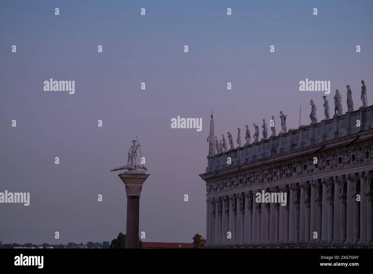 Blick auf die Piazzetta San Marco Säule Saint Theodore und klassische Statuen auf der Balustrade der Biblioteca Nazionale Marciana vor einem blauen Himmel Stockfoto