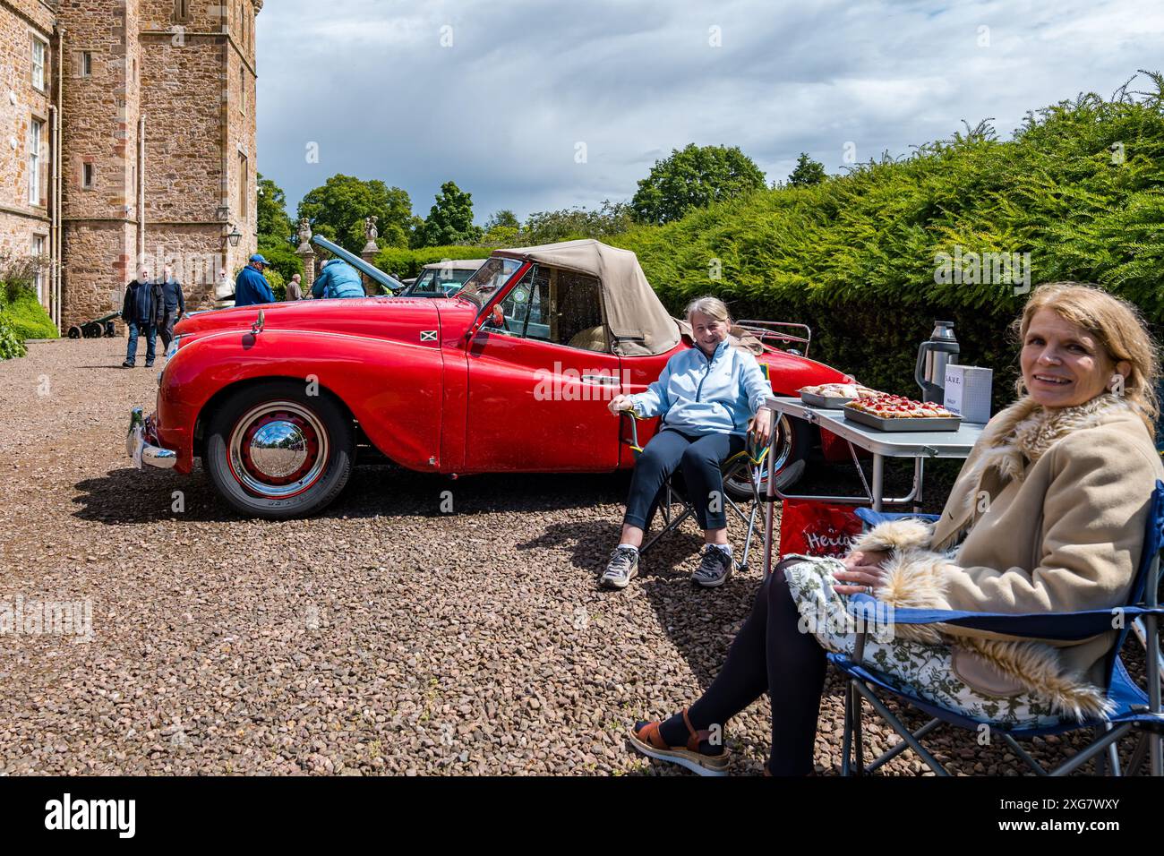 East Lothian, Schottland, Großbritannien, 7. Juli 2024. Räder der Vergangenheit: Die schottische Vereinigung der Fahrzeugliebhaber führt die Besitzer von Oldtimern durch die Landschaft zum malerischen Gelände des Lennoxlove House. Im Bild: Ruby und Carol, Jowett Jupiter Besitzer, gebackene Kuchen für die Teilnehmer. Quelle: Sally Anderson/Alamy Live News Stockfoto