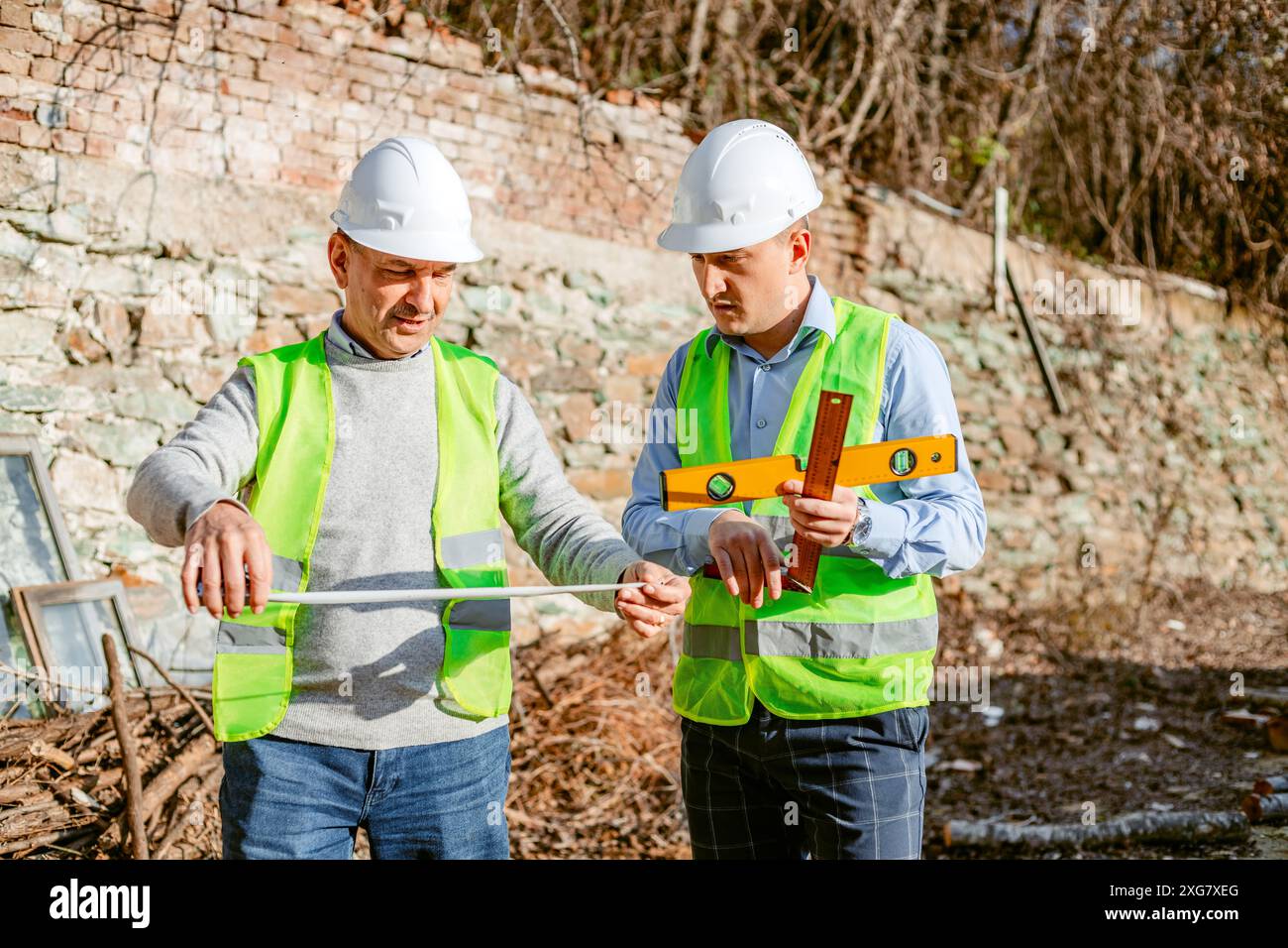 Zwei Bauarbeiter mit Schutzhüten und Sicherheitswesten arbeiten an einem Bauprojekt. Ein Arbeiter hält ein Maßband und verlängert sich Stockfoto