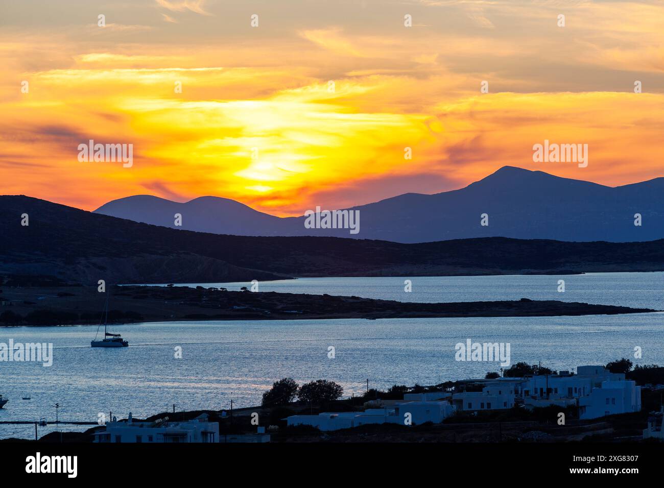 Atemberaubender Sonnenuntergang über dem ruhigen Wasser und den zerklüfteten Hügeln der Insel Antiparos, Griechenland, der ein warmes Licht über die Landschaft wirft. Stockfoto