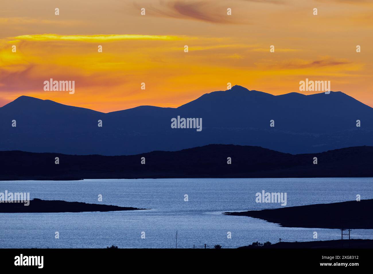 Atemberaubender Sonnenuntergang über dem ruhigen Wasser und den zerklüfteten Hügeln der Insel Antiparos, Griechenland, der ein warmes Licht über die Landschaft wirft. Stockfoto