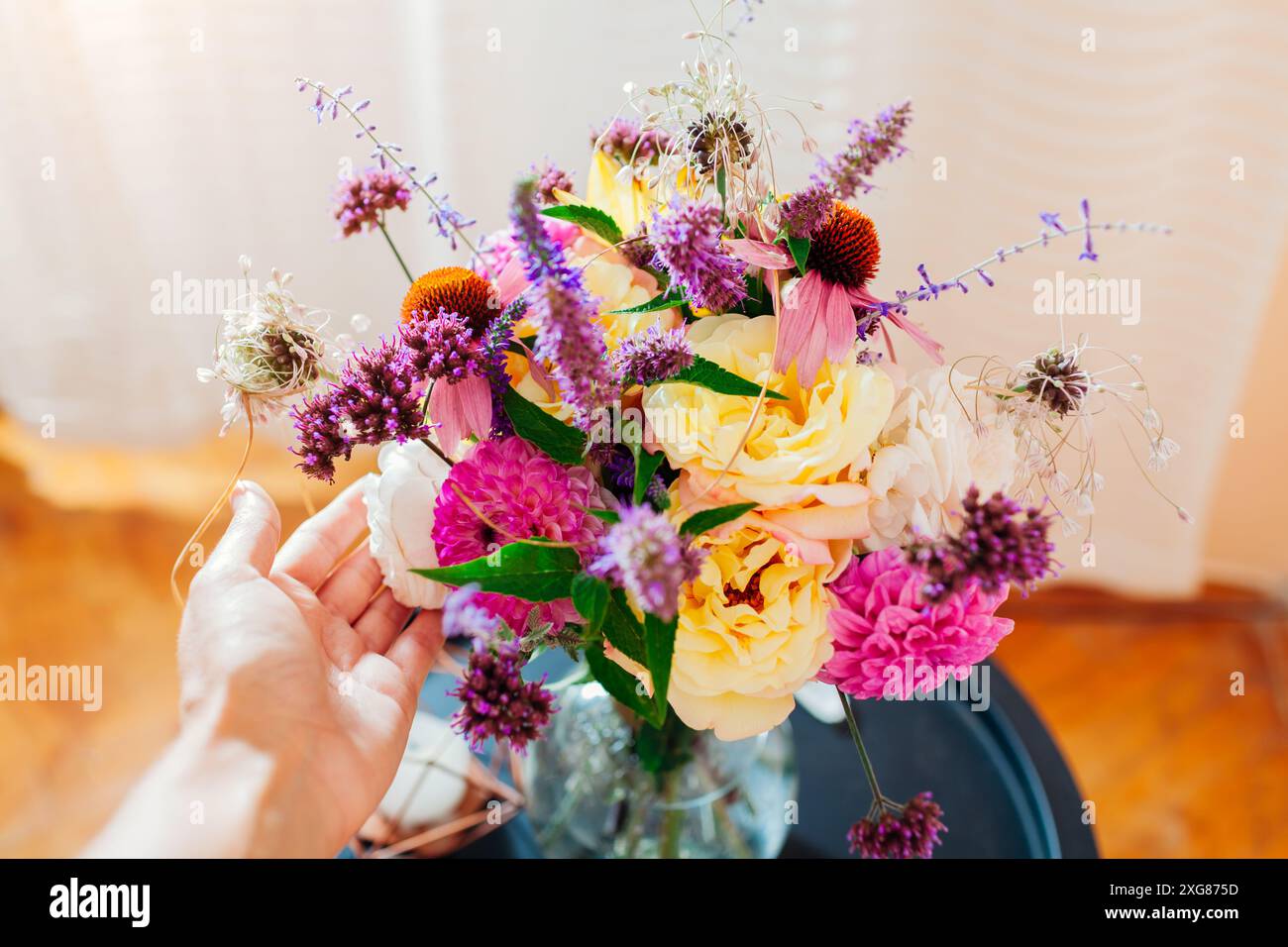 Blick von oben auf den frischen Sommerstrauß in der Vase auf dem Tisch. Rosa, gelbe, lila Blüten. Frau genießt Blumenarrangements aus Dahlien, Rosen, Eisenkraut, V Stockfoto