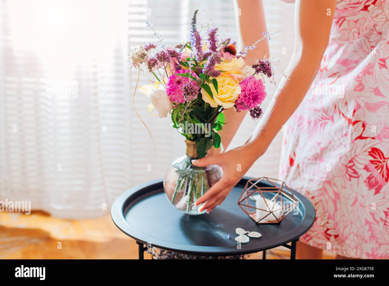 Frau legt Blumenstrauß in Vase auf Couchtisch zu Hause. Lieferung von frischen Blumenarrangements der Saison für die Inneneinrichtung. Nahaufnahme Stockfoto