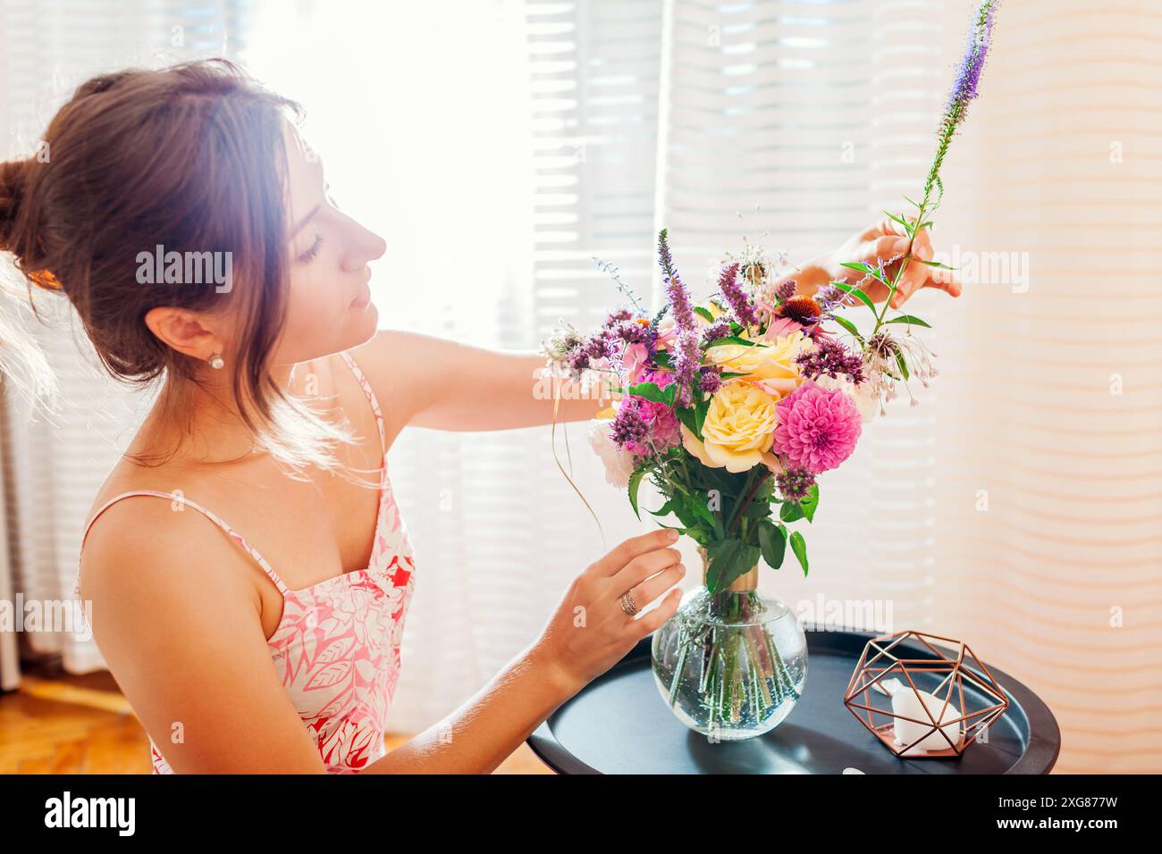 Die junge Frau arrangiert einen Blumenstrauß aus Sommerblumen in einer Vase zu Hause, die morgens auf einen Kaffeetisch gestellt wird. Inneneinrichtung und Einrichtung Stockfoto