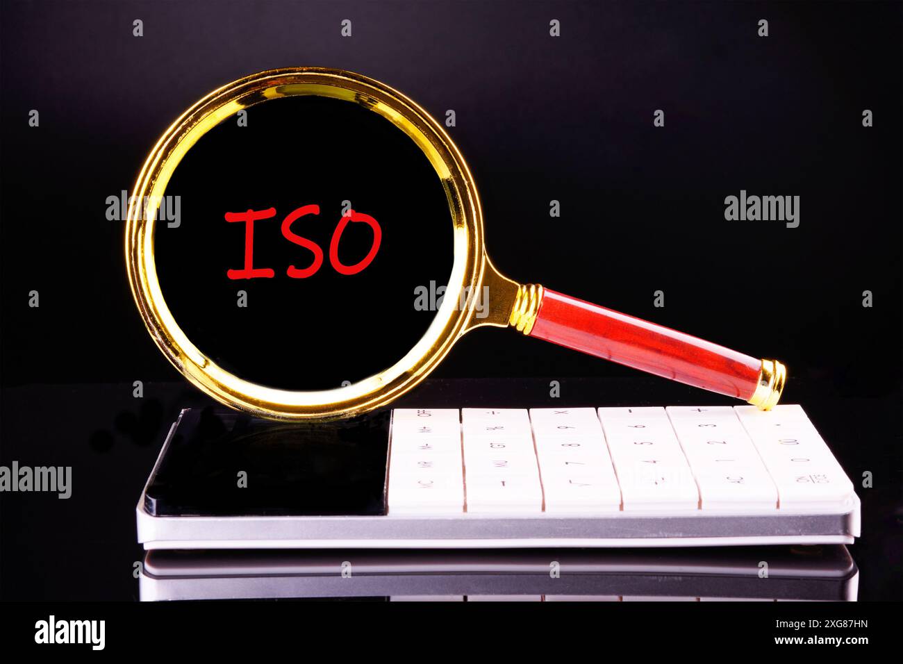Die Abkürzung ISO wird durch eine Lupe auf einem Rechner auf schwarzem Hintergrund geschrieben Stockfoto