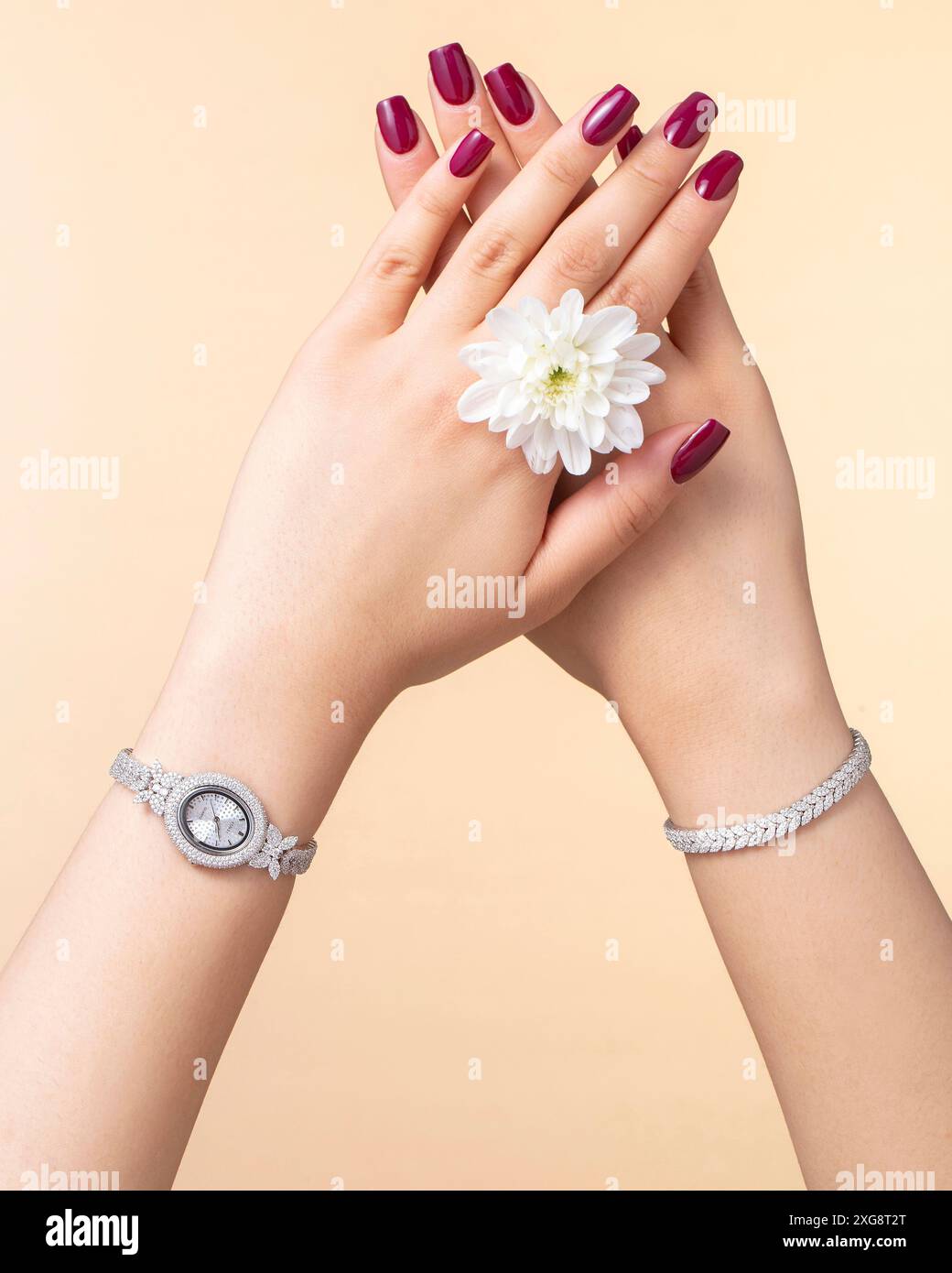 Nahaufnahme einer Damenhand mit einer diamantbesetzten Uhr und einem Armband vor einem weichen beigefarbenen Hintergrund mit luxuriösen Modeaccessoires Stockfoto