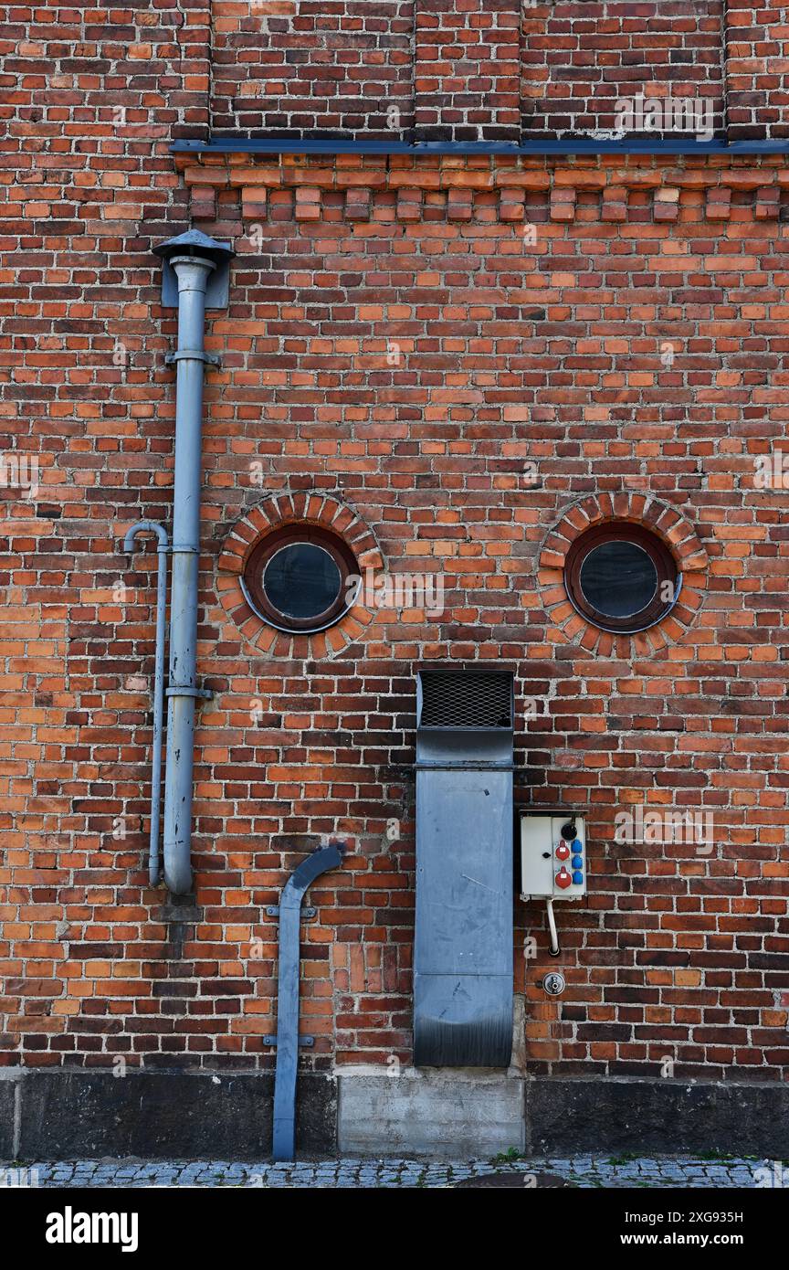 Ziegelwand einer alten Fabrik mit runden Fenstern und Lüftungsrohren Stockfoto