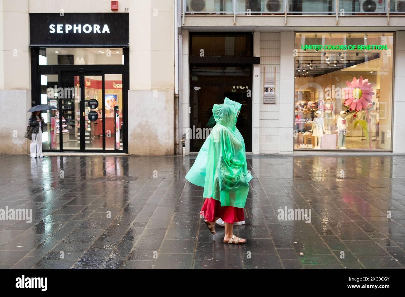 Zwei Frauen mit grünen Regencapes gehen an einem United Colours of Benetton im Regen in Bari, Apulien, Italien vorbei Stockfoto