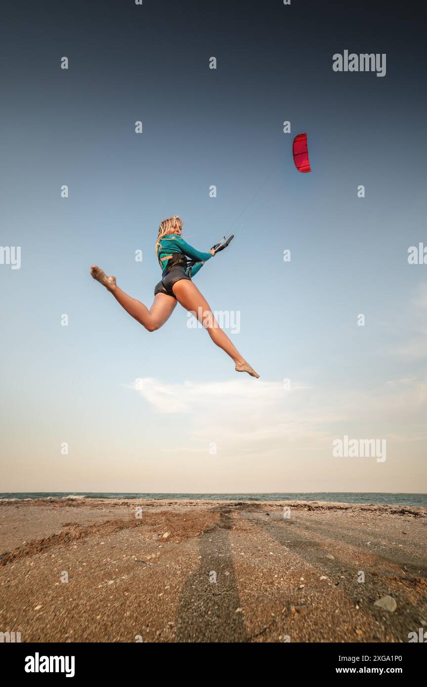 Sportlerin Kitesurferin springt mit ihrem Drachen am Strand. Kostenloser Flug über Land mit einem Drachen Stockfoto