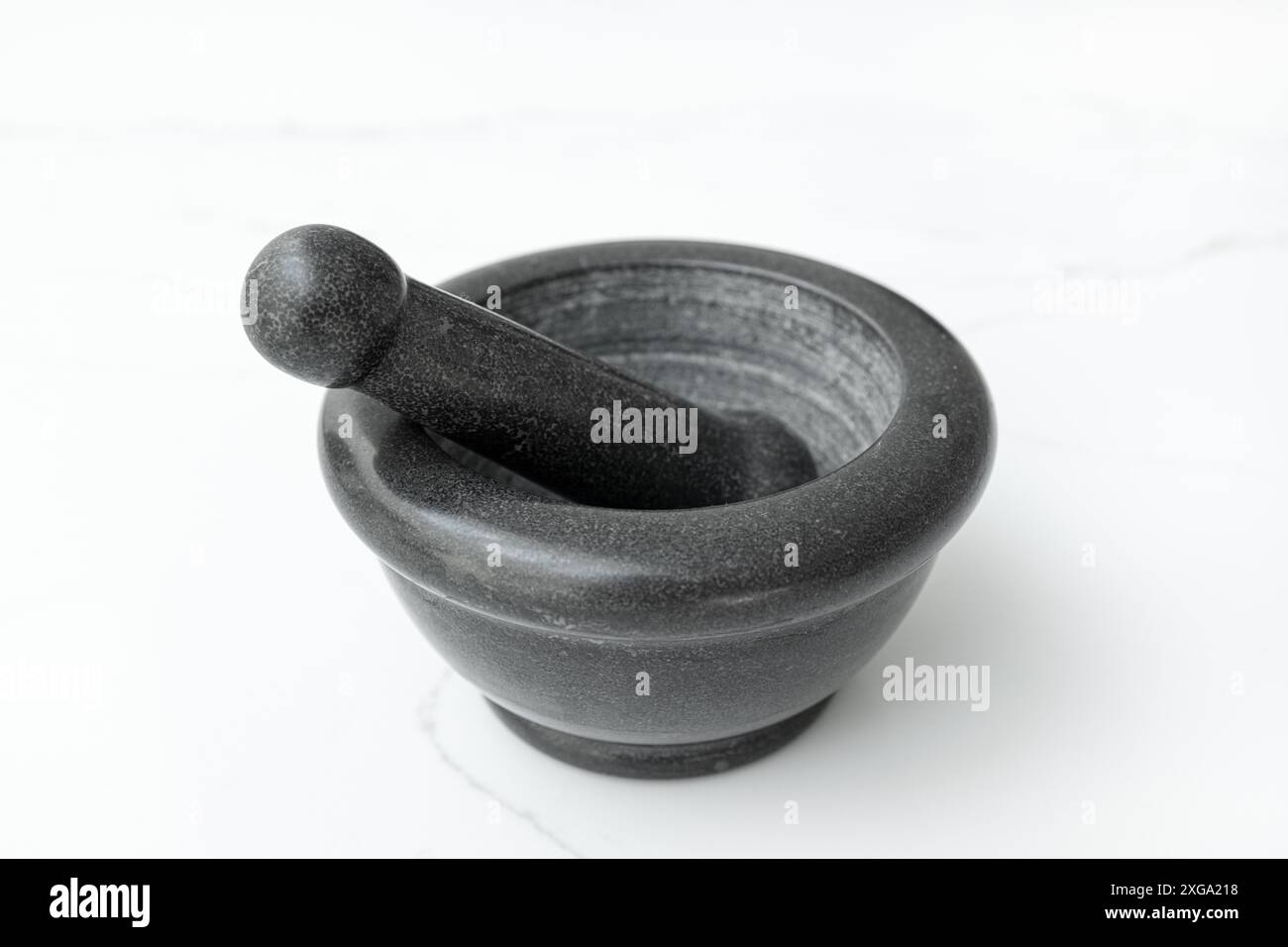 Schwarzer Steinmörtel und Stößel isoliert auf weißem Marmortisch Stockfoto