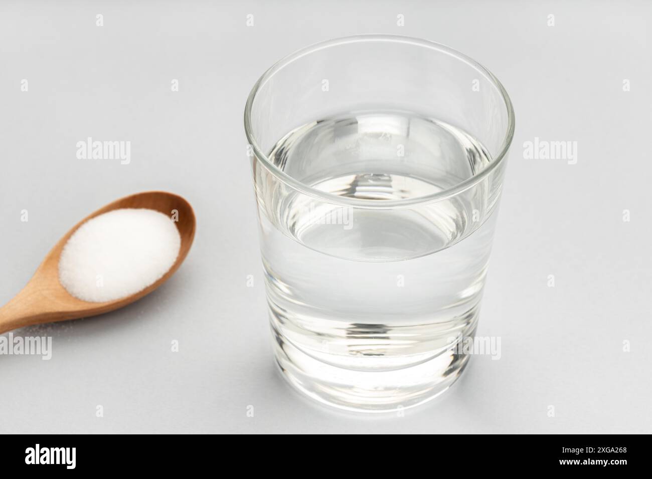 Glas Wasser und Backsoda in Holzlöffel isoliert auf grauem Hintergrund Stockfoto