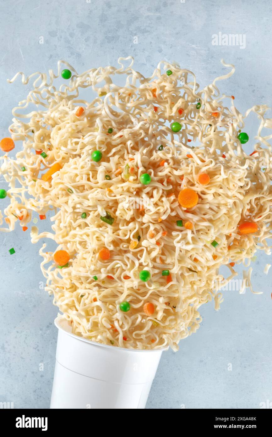Ramen Tasse mit Instant-Nudeln fliegen aus ihm. Nudelgericht mit Karotte und grünen Erbsen, eine Nahaufnahme Stockfoto