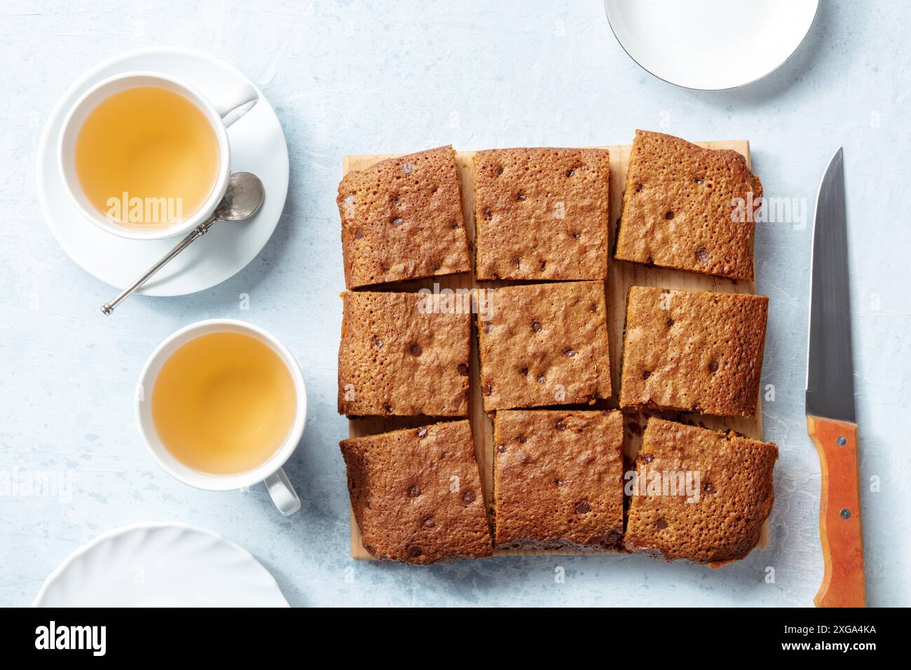 Blondie Brownie Dessertbars mit Schokoladenstückchen, darüber liegende flache Lay Shot mit Tassen Tee Stockfoto