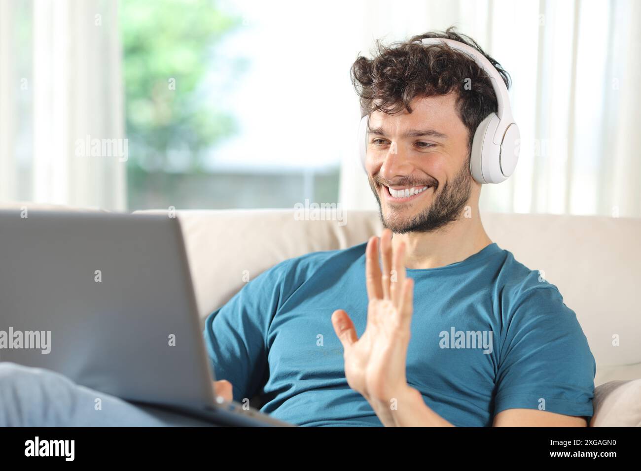 Glücklicher Mann, der Videoanrufe auf einem Laptop hat und zu Hause auf einer Couch sitzt Stockfoto