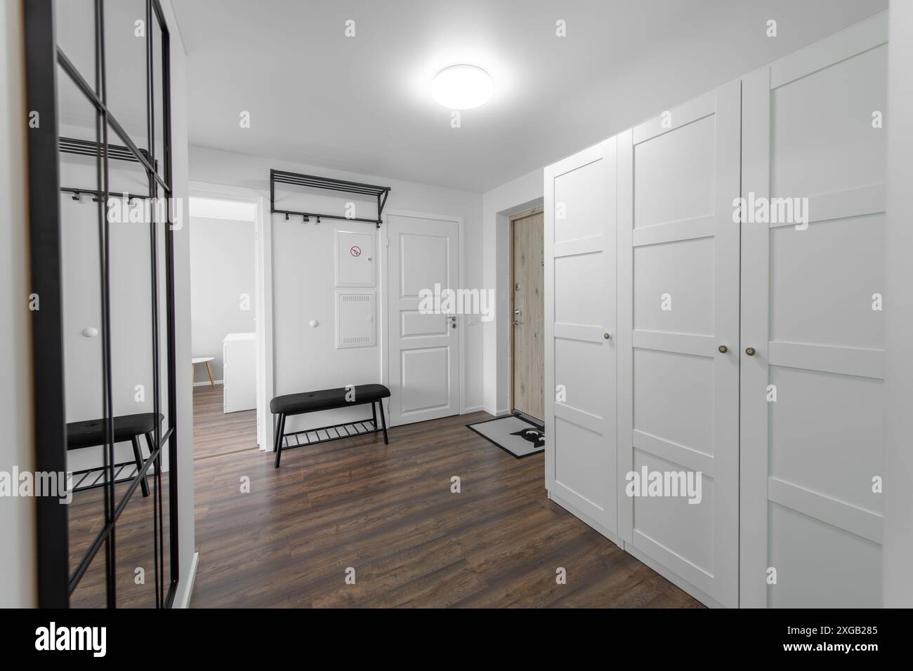 Eingangsbereich Zu Hause. Innenraum. Weiße Holztür, brauner Boden und weißer Kleiderschrank. Minimalismus. LED-Leuchte. Schwarze Bank Stockfoto