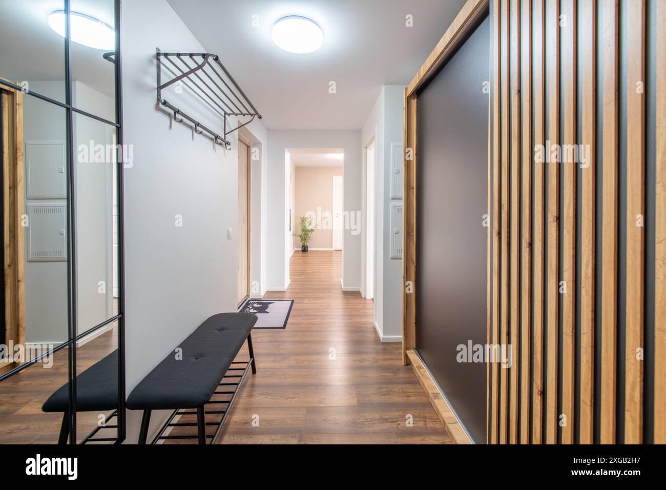 Eingangsbereich Zu Hause. Innenraum. Weiße Holztür, brauner Boden und weißer Kleiderschrank. Minimalismus. LED-Leuchte. Schwarze Bank. Spiegeln Stockfoto