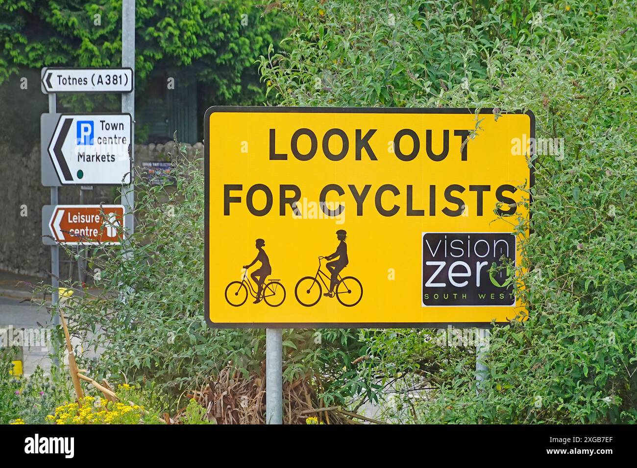Halten Sie Ausschau nach Radfahrern. Ein deutliches gelbes Straßenschild an der Kreuzung des Kreisverkehrs ist ein multinationales Projekt der Vision Zero zur Verkehrssicherheit in England Großbritannien Stockfoto