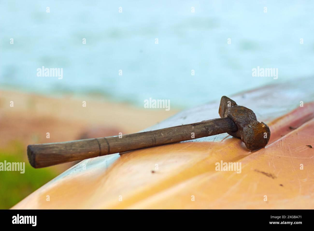 Ein alter rostiger Hammer liegt auf dem Plastikrumpf des Bootes im Hintergrund des Wassers Stockfoto