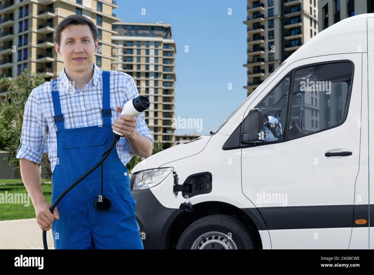 Mann in Uniform hält den Ladestecker für Elektrofahrzeuge. Elektrobus im Hintergrund. Stockfoto