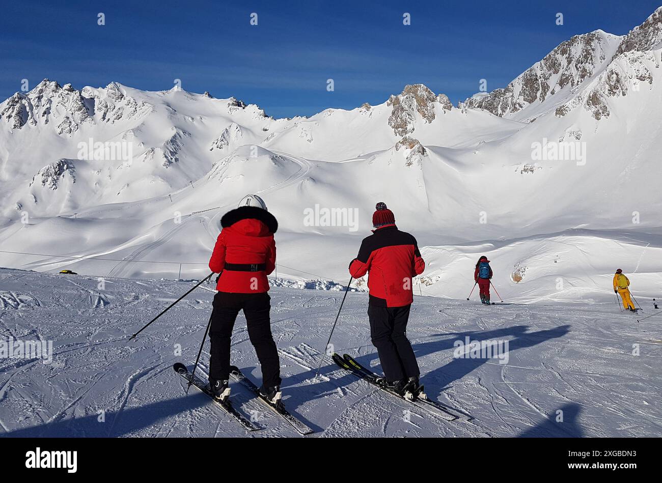 Zwei Skifahrer stehen auf einer Skipiste oberhalb von Tignes in Frankreich bereit, in roten Skijacken abzusteigen und von der Kamera wegzusehen. Stockfoto