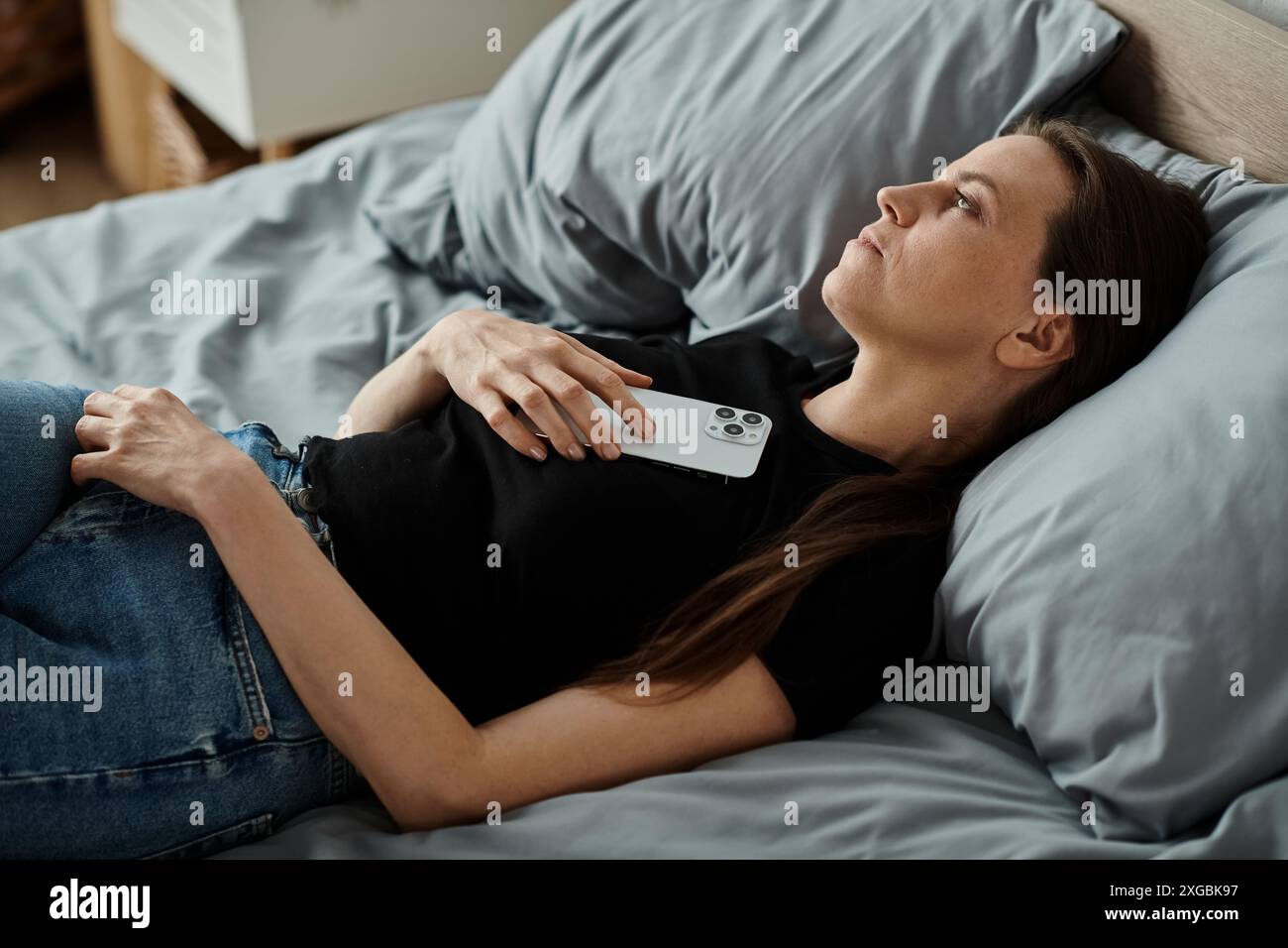 Eine Frau im Bett mit ihrem Telefon, die sich intensiv mit der digitalen Verbindung beschäftigt. Stockfoto
