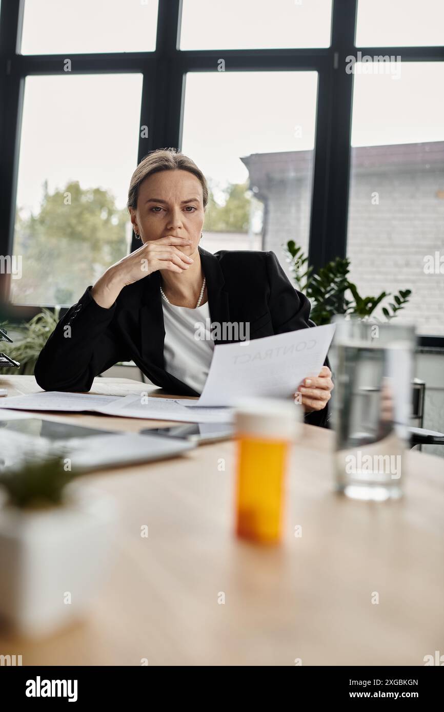 Eine Frau mittleren Alters sitzt an einem Tisch und untersucht aufmerksam ein Blatt Papier. Stockfoto