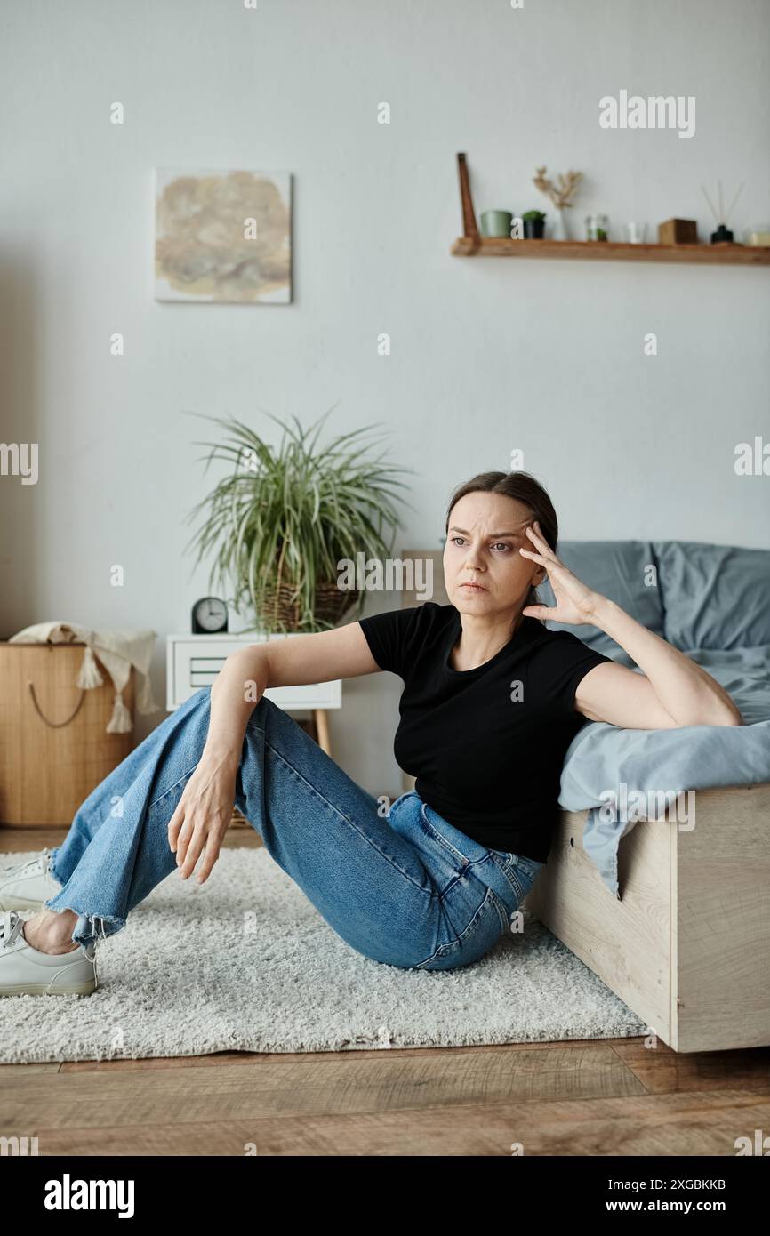 Eine Frau mittleren Alters, die Einsamkeit und Besinnung annimmt, während sie auf dem Schlafzimmerboden sitzt. Stockfoto