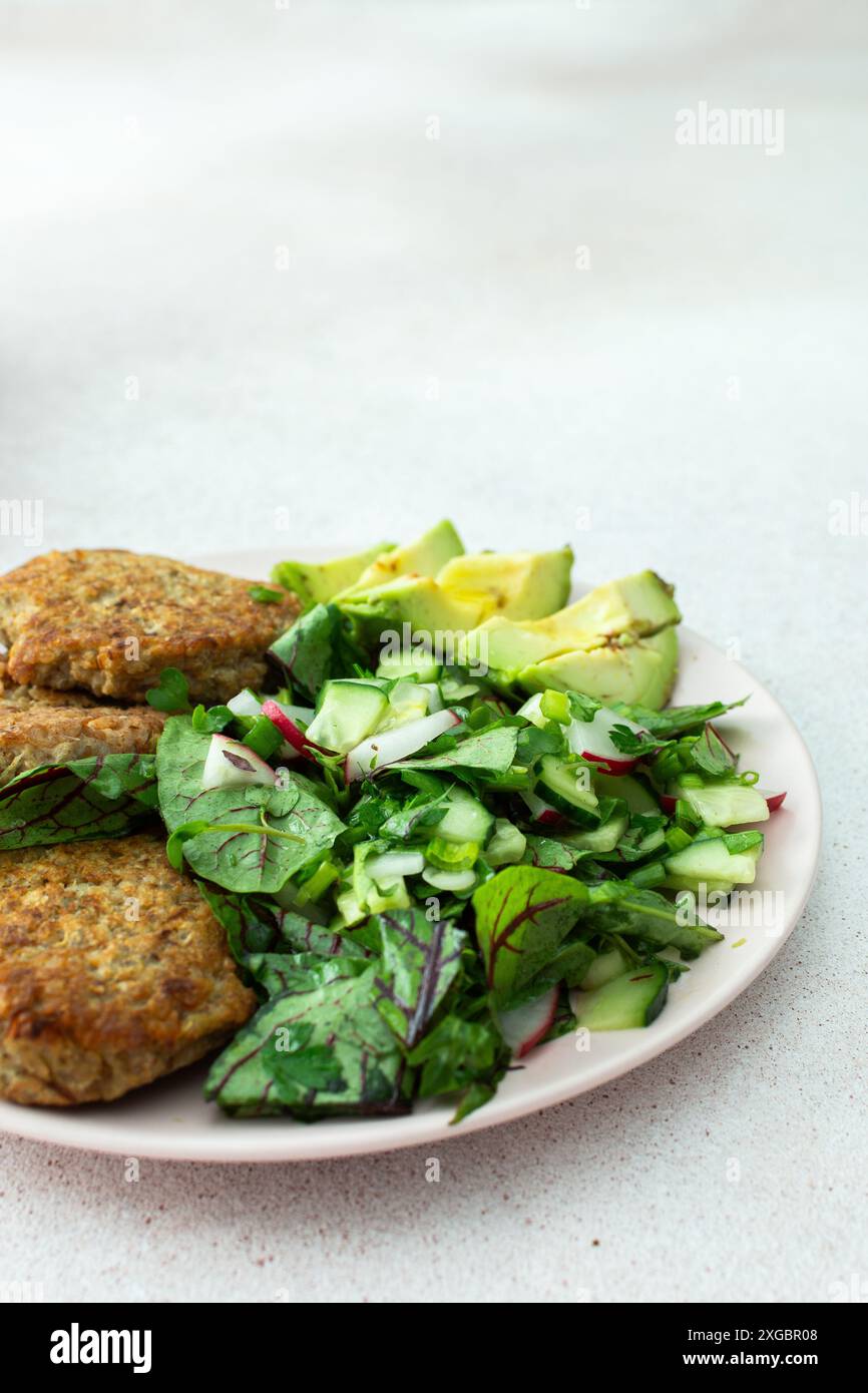 Quinoa-Schnitzel und gemischter Salat mit Avocado und Radieschen, Kiwi und Wasser mit Zitrone, köstliches herzhaftes Frühstück, veganer Lunch-Teller Stockfoto