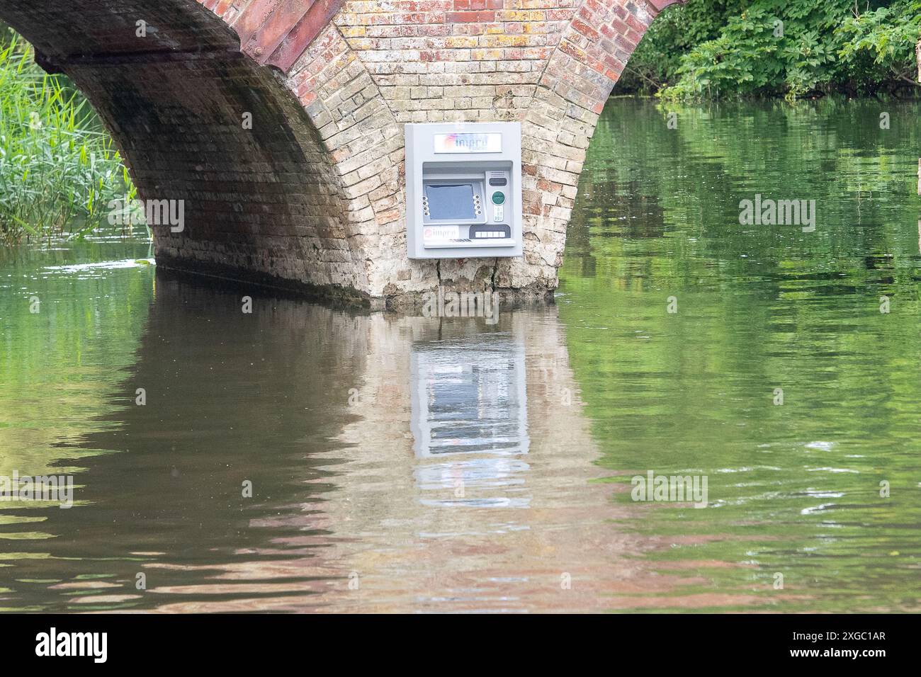 Sonning-on-Thames, Berkshire, Großbritannien. Juli 2024. Ein Streich namens Impro hat an der Wand der Sonning Bridge oberhalb der Themse in Sonning-on-Thames, Berkshire, einen Geldpunkt platziert. Über dem Cashpoint befindet sich ein Impro Solutions Logo. Impro war auch hinter einem Briefkasten, der vor ein paar Monaten an derselben Mauer über der Themse angebracht wurde. Dies hat den Einheimischen viel Spaß bereitet und das Ziel soll darin bestehen, die Aufmerksamkeit auf die Anzahl der Banken zu lenken, die geschlossen werden. Berühmte Bewohner, die Eigentum in Sonning besitzen, sollen George Clooney und der ehemalige P sein Stockfoto