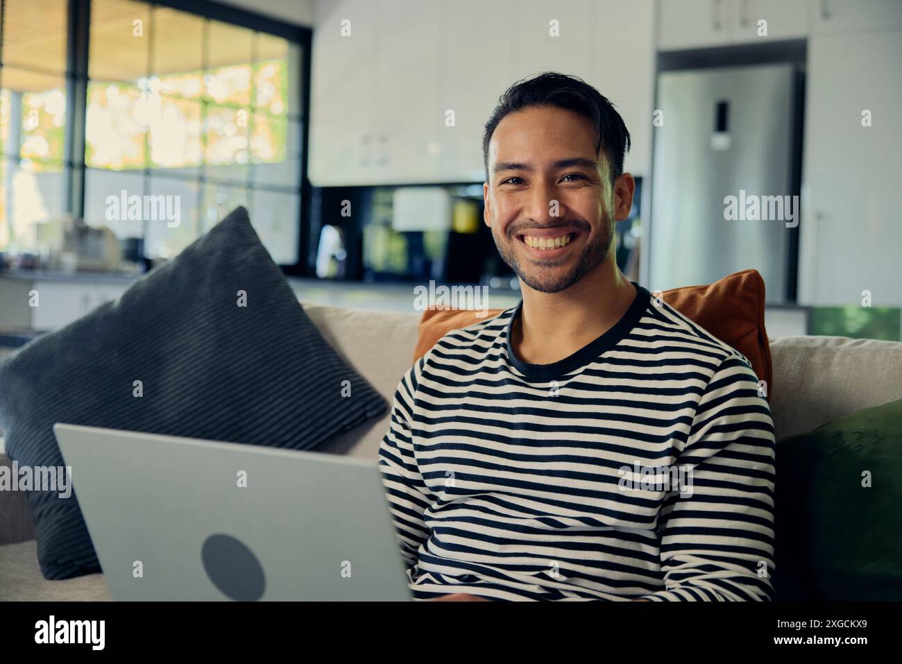 Ein Mann in einem Smiley-T-Shirt benutzt einen Laptop auf einer Couch in einem Haus Stockfoto