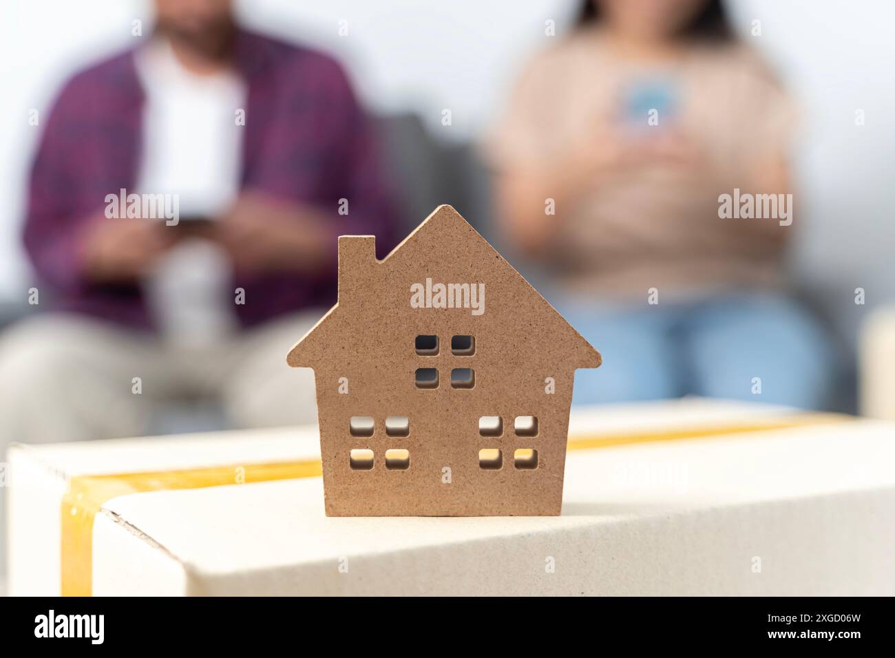 Ein junges Paar nutzt ein Smartphone, um Informationen über den Umzug zu finden. Männlich und weiblich und Hausmodell. Hausplan auf Pappkarton am Umzugstag, c Stockfoto