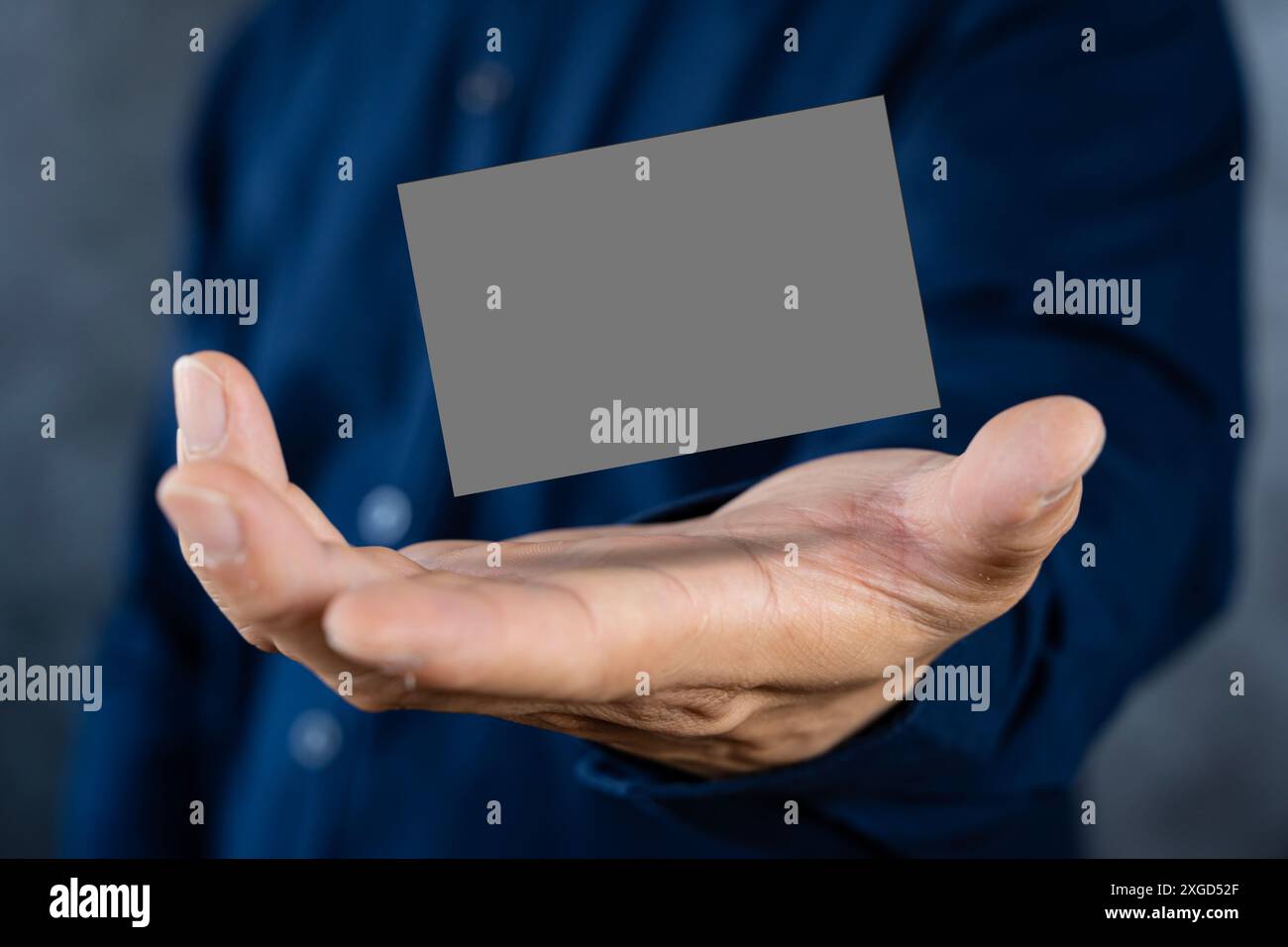Mann, der eine dunkelgraue Visitenkarte gegen eine Betonwand hält Reife männliche Hand, die eine leere Visitenkarte vor der Kamera hält. Verschwommener Hintergrund Stockfoto