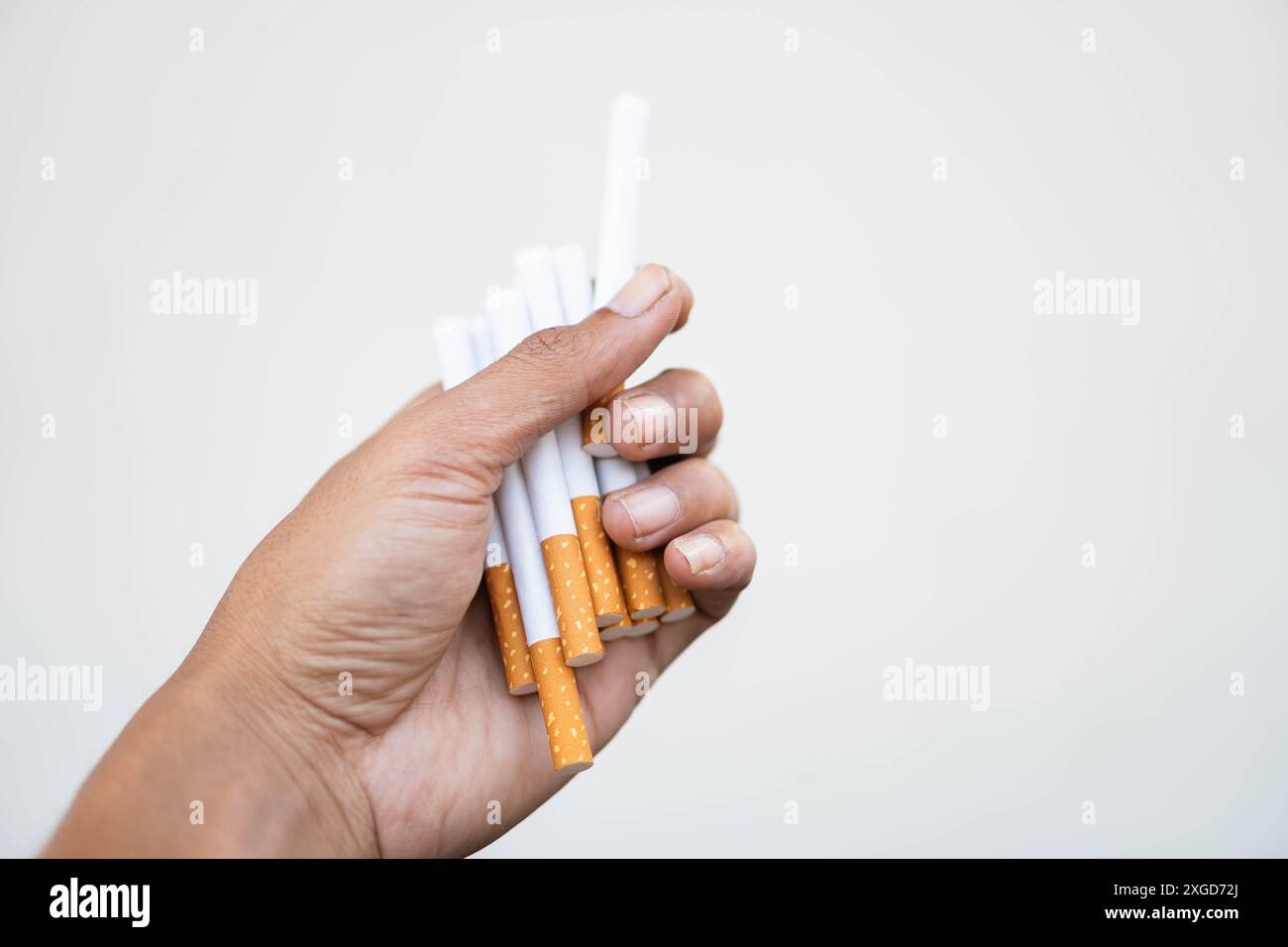 Eine Nahaufnahme einer Hand, die einen Haufen Zigaretten vor einem einfachen Hintergrund hält. Stockfoto