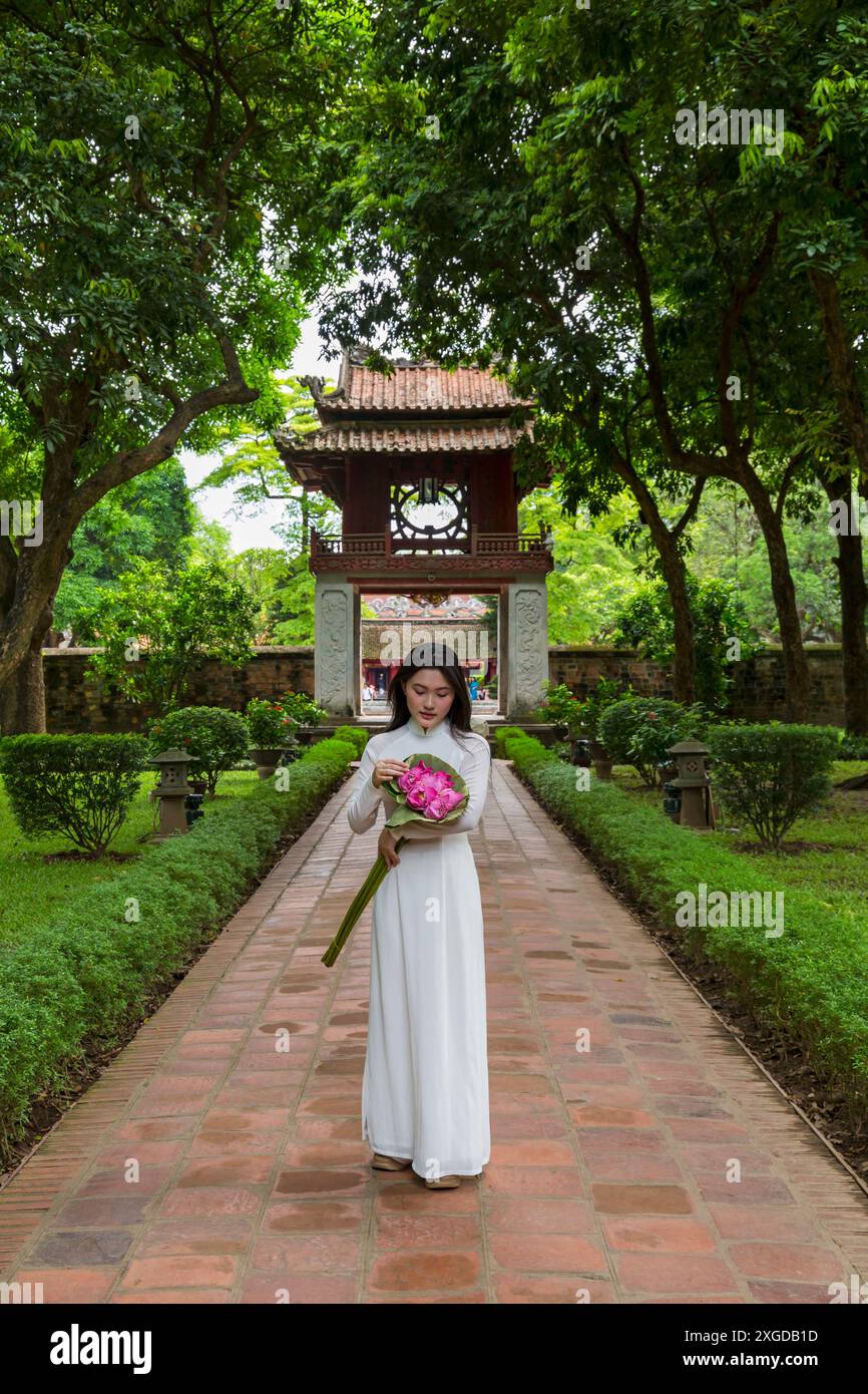 Hübsche vietnamesische junge Frau in traditioneller Ao Dai Tunika mit Lotusblumen im Literaturtempel in Hanoi, Nordvietnam, Asien Stockfoto