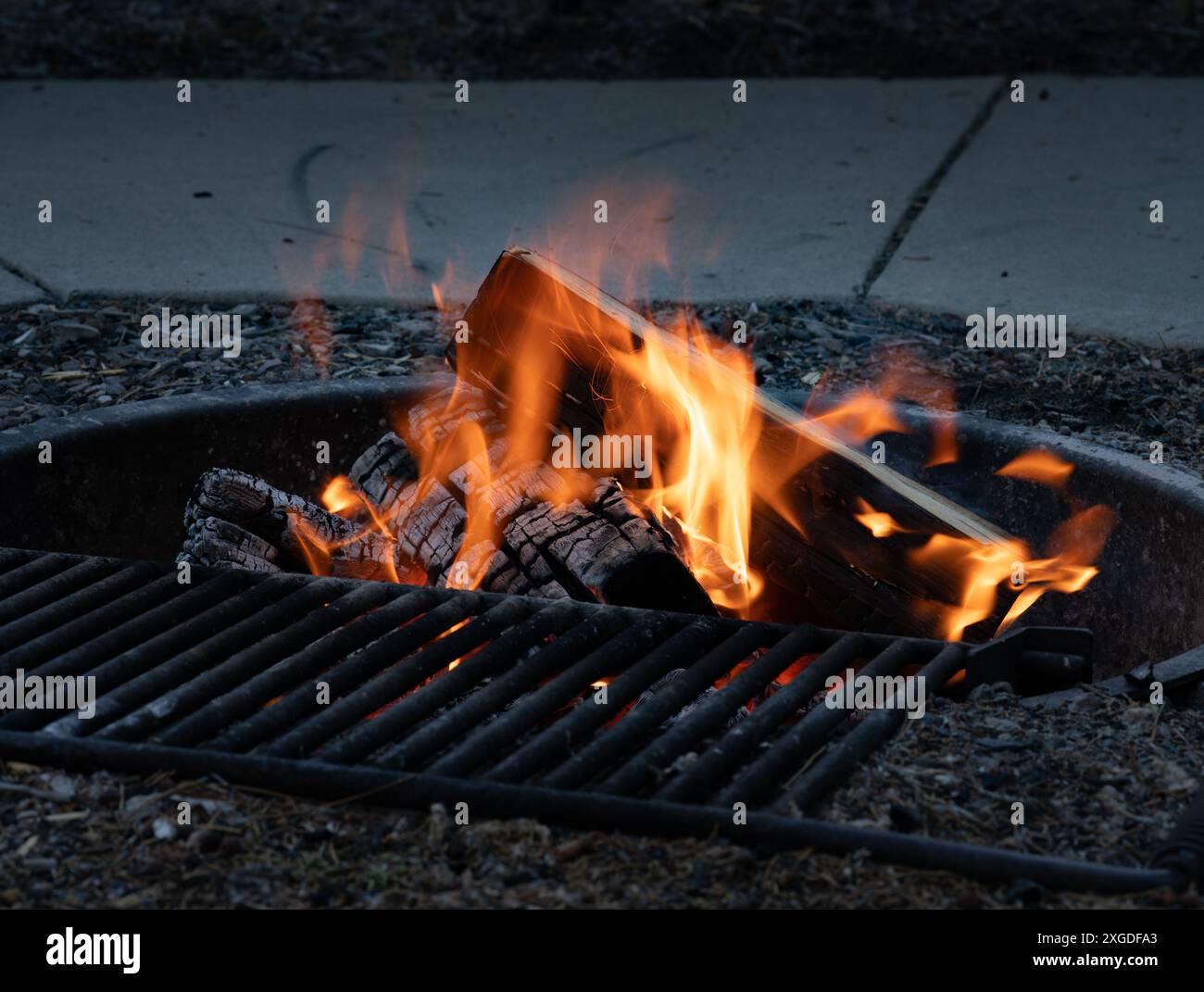 Feuerstelle auf dem Campingplatz mit brennenden Stämmen und Stahlgitter zum Kochen über offener Flamme Stockfoto