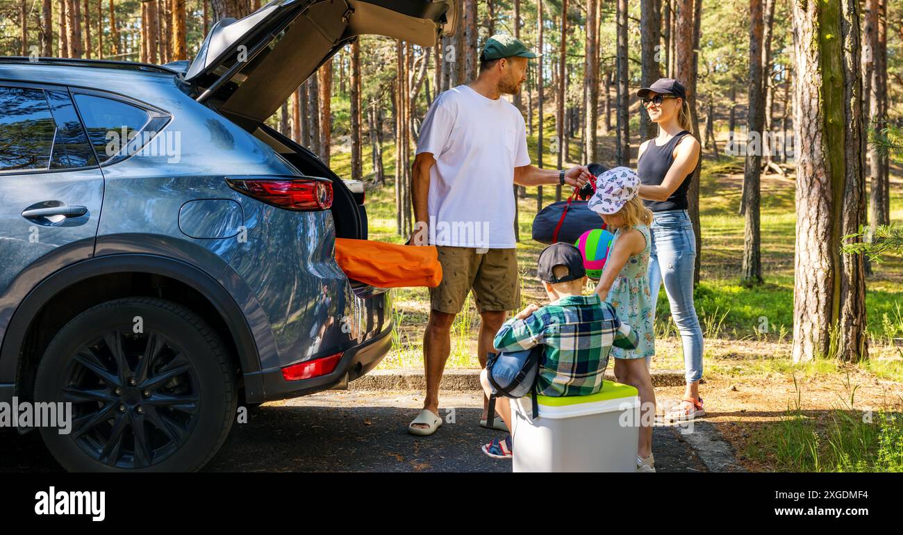 Familie mit Kindern entfernt die Campingzubehör aus dem Kofferraum im Wald. Sommerurlaub, Roadtrip Stockfoto