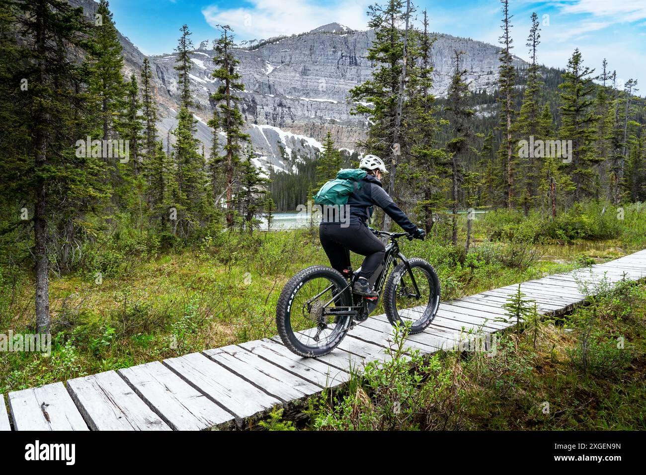 Lake Louise Alberta Canada, 24. Juni 2024: Radfahrer fahren mit dem Fahrrad über eine hölzerne Promenade mit Blick auf den Gletschersee am Fuße eines Berges in Banff Natio Stockfoto