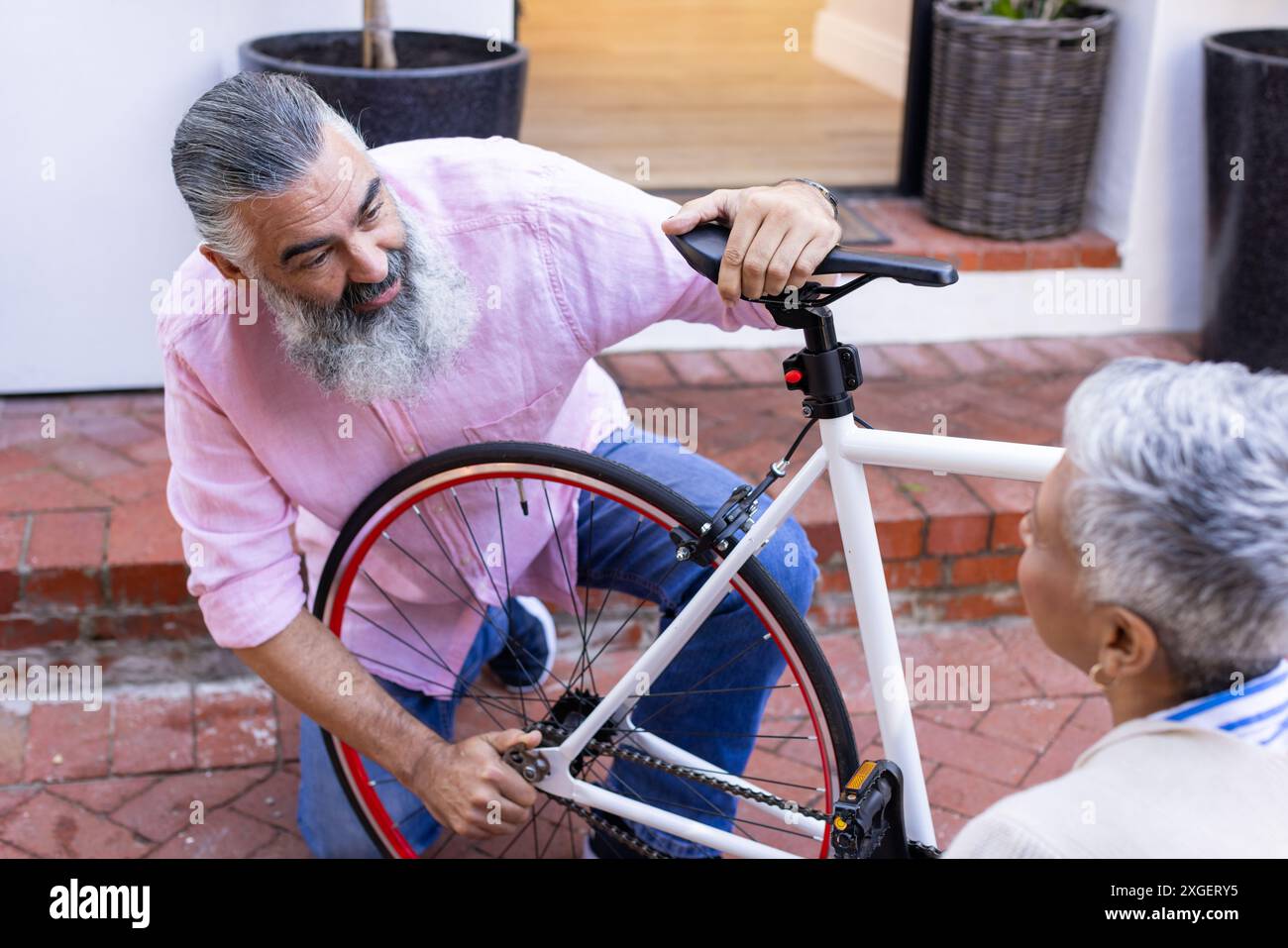 Fahrrad reparieren, Seniorenmann, der den Sitz verstellt, während er draußen mit der Frau spricht Stockfoto