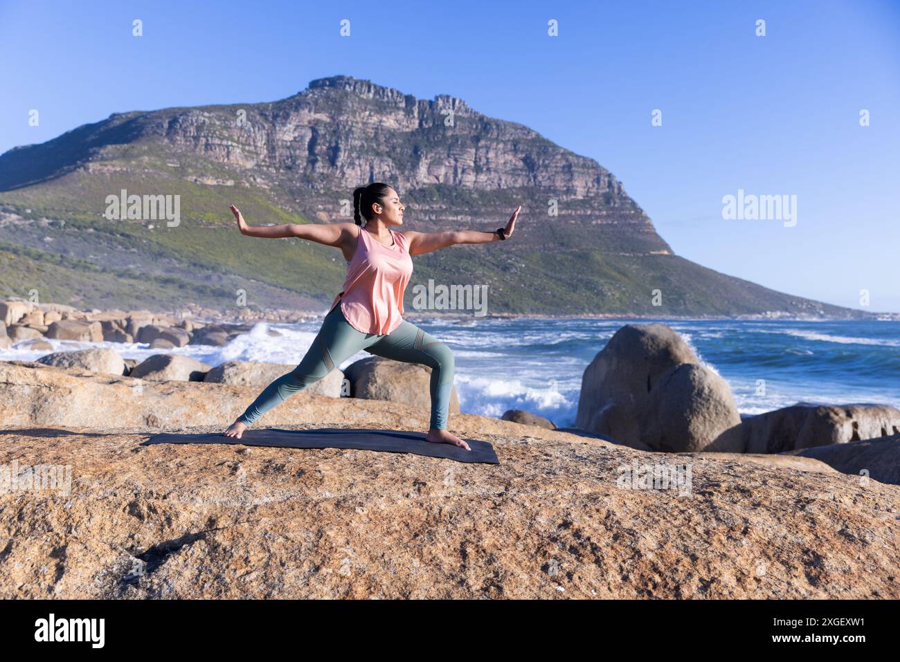 Yoga auf Matte üben, reife Frau, die Kriegerposen an den Klippen des Ozeans macht, Kopierraum Stockfoto