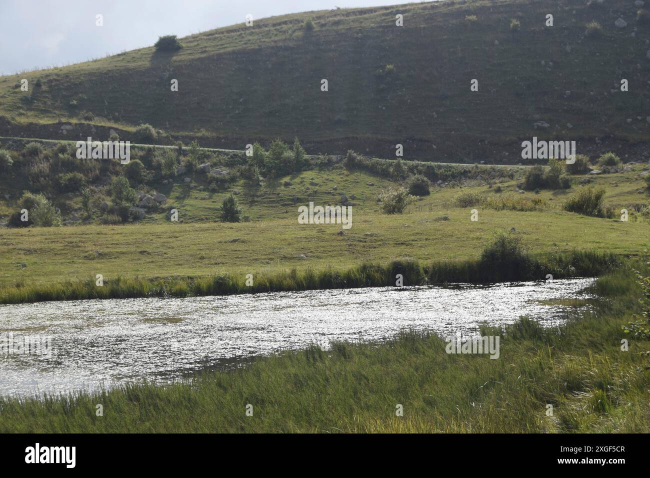 Ein ruhiger Teich umgeben von grasbewachsenen Hügeln auf dem Land Stockfoto